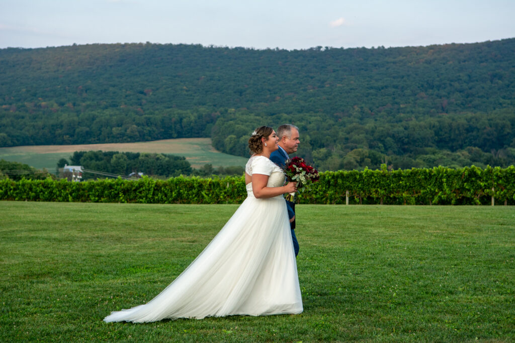 A bride and groom walking in the grass.