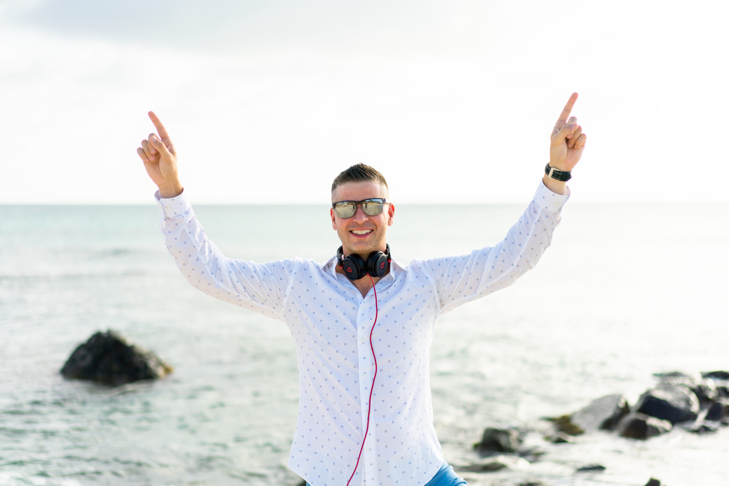 A man with headphones on standing in front of the ocean.