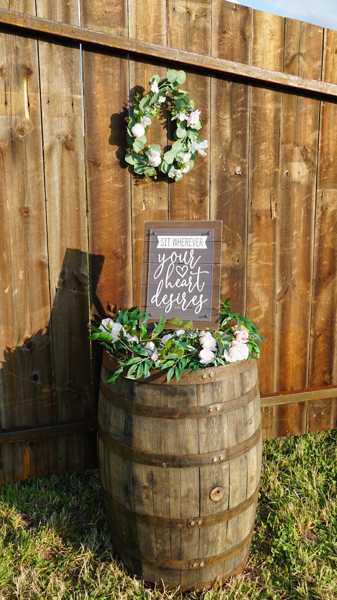 A wooden barrel with flowers and a sign on top of it.