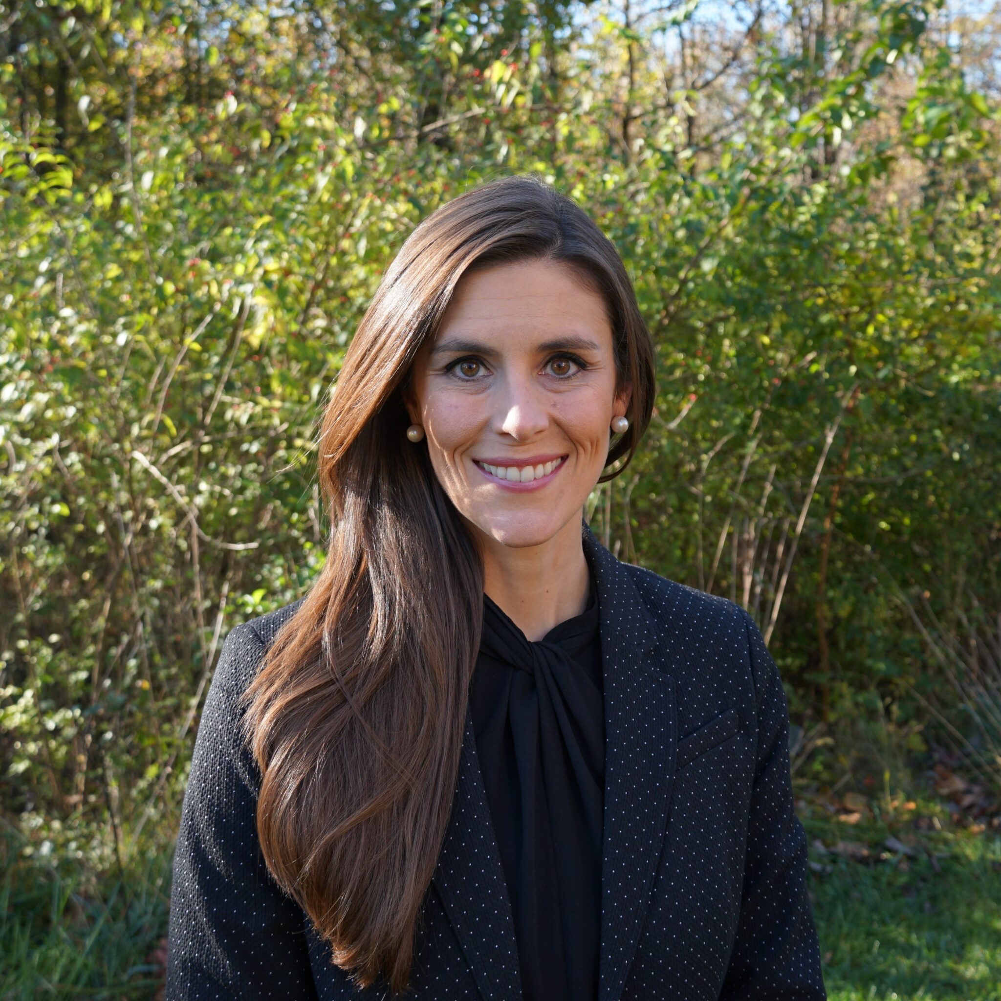 A woman in black jacket standing next to trees.