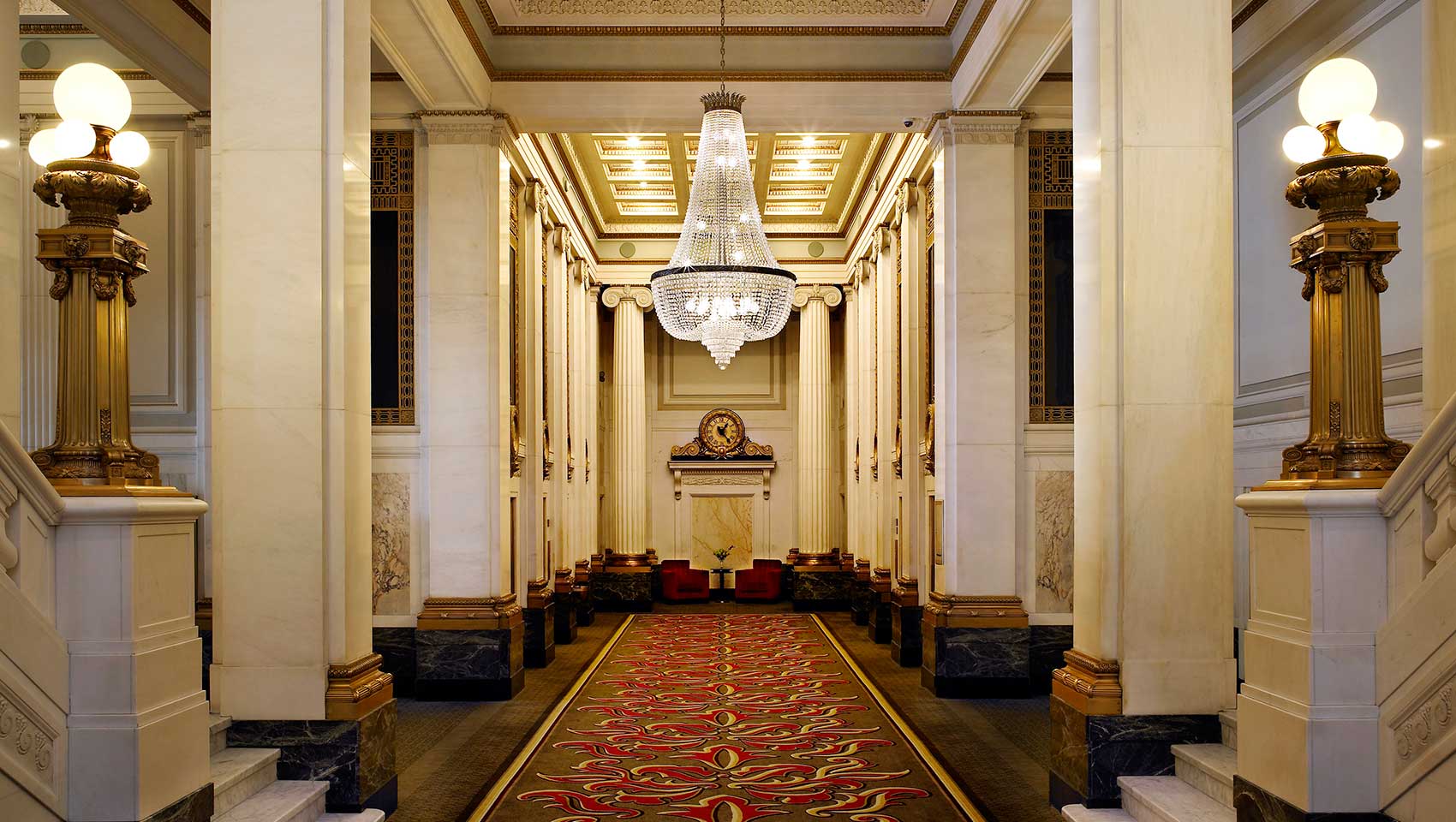 A long hallway with pillars and a chandelier.