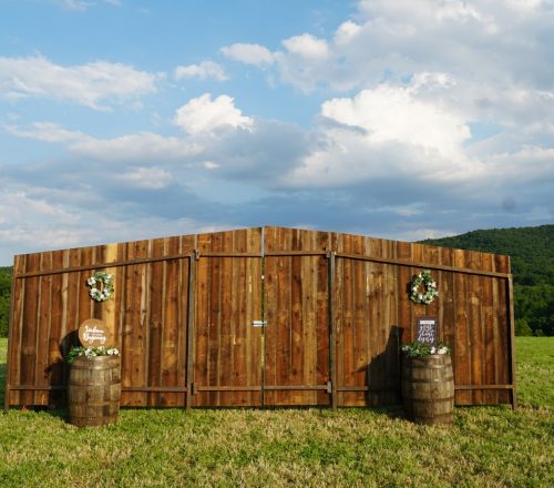 A wooden fence with two barrels in the grass.